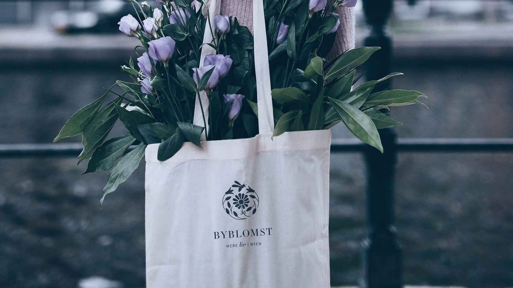 Et stofnet fyldt med grønne blomster. På siden af nettet er logoet fra tegnestuen Byblomst med små blomster og en bi