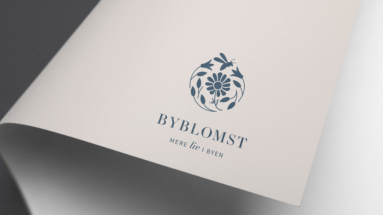 Mockup af trykt brochure for Byblomst med det blå logo på sandfarvet baggrund