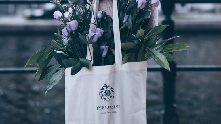 Et stofnet fyldt med grønne blomster. På siden af nettet er logoet fra tegnestuen Byblomst med små blomster og en bi